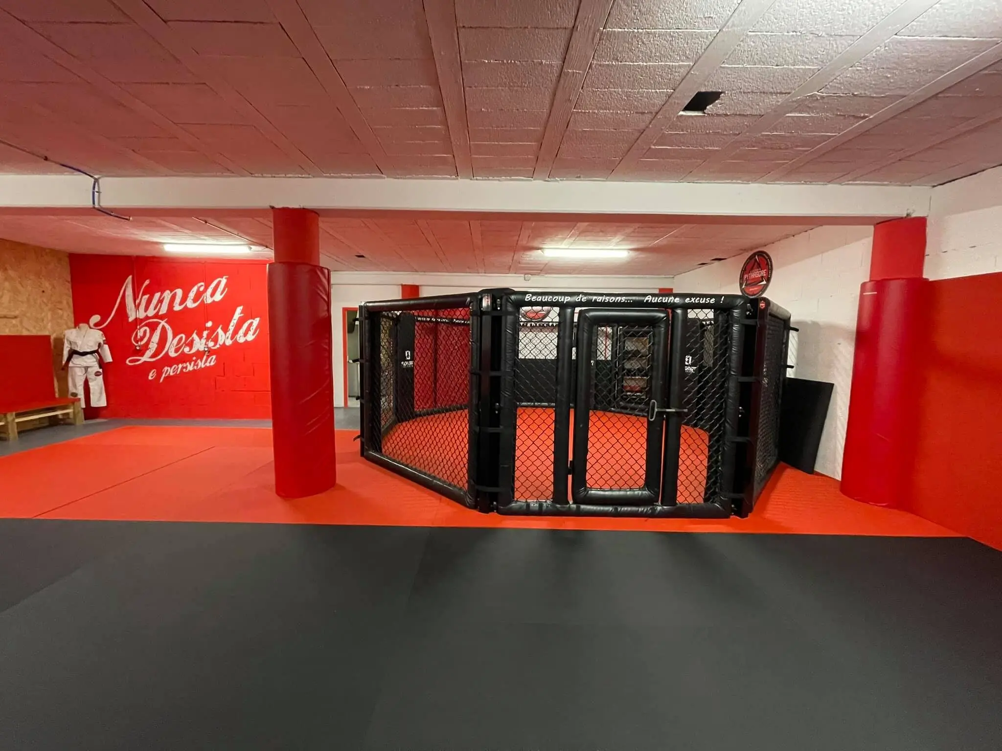 Le dojo de l’Académie Pythagore à Angoulême : tatamis rouges et noirs, la cage de MMA et le mur peint « Nunca Desista ».
