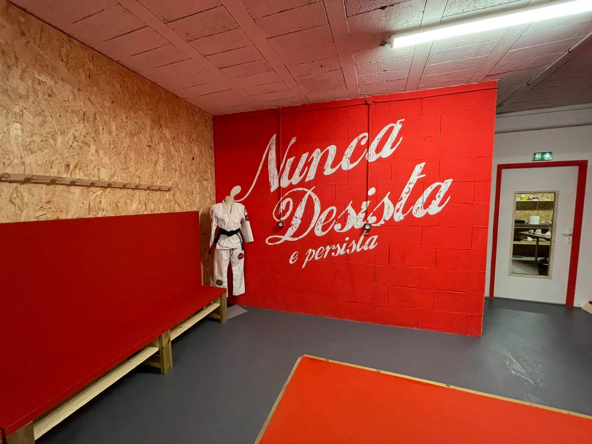 Le mur rouge du dojo, peint de la devise « Nunca Desista, e persista », avec un kimono à ceinture noire sur un mannequin.